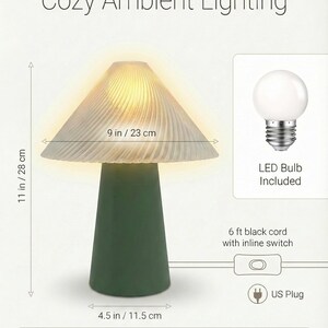 May include: A mushroom-shaped table lamp with a green base and a ribbed, off-white shade. The lamp is 11 inches tall and 9 inches wide. It includes an LED bulb and has a 6 ft black cord with an inline switch. The text "Cozy Ambient Lighting" is at the top.