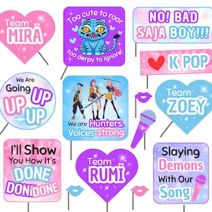 May include: A collection of colorful photo booth props with various designs and text. The props include heart-shaped signs with names, speech bubbles, and signs with phrases like "Too cute to roar" and "Slaying Demons With Our Song."