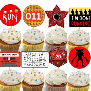 May include: Cupcakes with white frosting and colorful sprinkles, topped with themed decorations. Decorations include the word "RUN", a waffle, the number "011", a Demogorgon, the text "I'M DONE RUNNING", a cassette tape, a string of lights with letters, and a red die.