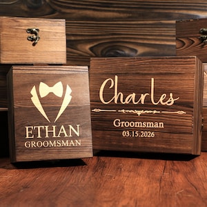 May include: Wooden boxes with engraved designs. One box features a tuxedo graphic and the name "Ethan, Groomsman." Another box is inscribed with "Charles, Groomsman, 03.15.2026." The boxes are stained a dark brown color.