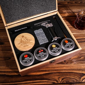Puede incluir: Un juego de caja de regalo de madera con piedras de whisky, un encendedor de soplete y virutas de madera con sabores de manzana, cereza, nuez y roble. La caja incluye un posavasos de madera con el nombre "JOSEPH" y el año "2025" grabados.