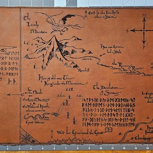 May include: A brown map with black illustrations and text, depicting a fantasy landscape with mountains, a river, and a dragon. The map includes text such as "The Lonely Mountain" and "The Desolation of Smaug."
