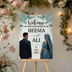 May include: An engagement sign on an easel reads "Welcome to the Engagement of Reema and Ali." The sign includes illustrations of a couple and the date, 27 November 2026. Floral arrangements and candles surround the sign.