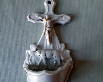 Peut inclure: Fontaine d'eau bénite murale en porcelaine blanche avec une croix et un agneau. La croix présente une figure dorée de Jésus-Christ.