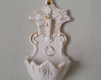 Peut inclure: Fontaine d'eau bénite en céramique blanche avec une bordure dorée et une représentation de Jésus sur la croix. La fontaine a une boucle en haut pour l'accrocher.