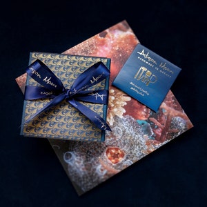 May include: A blue gift box with a gold and blue patterned design, tied with a blue ribbon and a gold tag that reads "Alison Moore Handmade in Orkney".