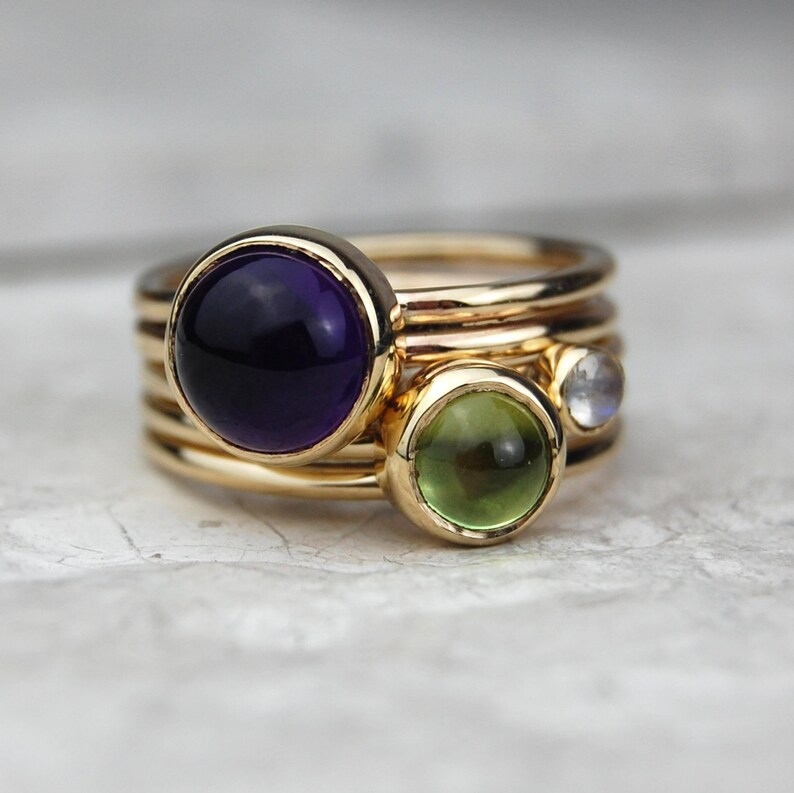 May include: A gold ring with three gemstones: a large purple amethyst, a smaller green peridot, and a tiny white moonstone.