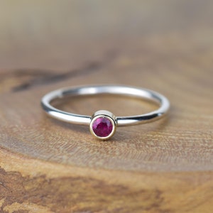 May include: A simple silver band ring with a small, round ruby gemstone set in a gold bezel.
