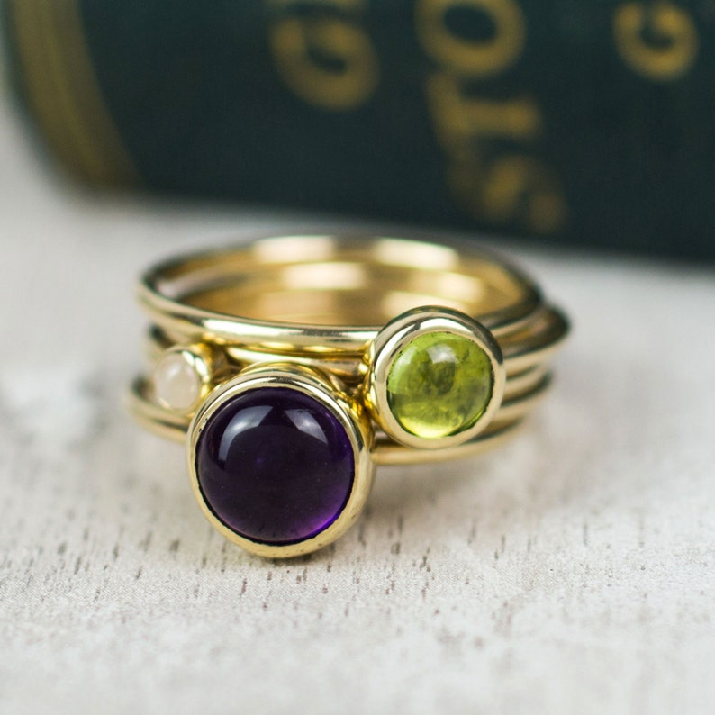 May include: A gold ring with three bands, featuring a purple amethyst, a green peridot, and a white pearl.
