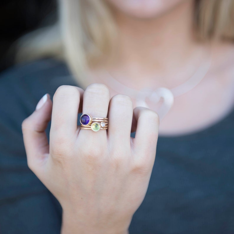 May include: A set of four gold rings with small gemstones. The rings feature a purple amethyst, a green peridot, and two clear white stones.