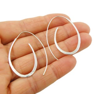 May include: A pair of silver-colored, open-hoop earrings. The earrings have a teardrop shape with a hammered texture on the outer edge. The hook extends from the top of the teardrop, creating a minimalist design.