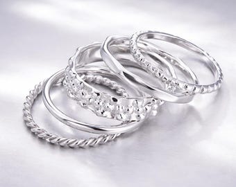 Juego de 5 anillos apilables plateados con texturas minimalistas.