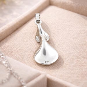 May include: A silver pendant with a teardrop design. The pendant is marked with "925" and is displayed in a jewelry box. The pendant has a loop at the top for a chain. The pendant is a shiny, reflective silver color.