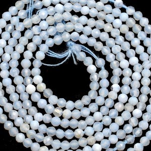 Puede incluir: Un collar de cuentas de piedras preciosas facetadas de color azul claro, dispuestas en espiral sobre un fondo negro. Las cuentas son pequeñas y redondas, con un brillo sutil. El hilo es de color azul claro a juego.