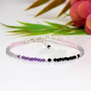 Puede incluir: Delicada pulsera de cuentas con una gradación de colores. La pulsera transiciona de rosa claro a gris, luego a morado y finalmente a cuentas negras. La pulsera está hecha con cuentas pequeñas y redondas y un cierre plateado.