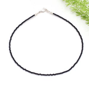 May include: A fine black beaded necklace with a silver clasp. The necklace is made up of tiny, round, black beads. The clasp is silver and fastens the two ends of the necklace together.