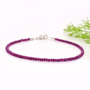 Op de afbeelding: Een fijne armband met kleine, gefacetteerde, dieproze edelstenen. De armband heeft een zilveren sluiting en wordt gepresenteerd tegen een witte achtergrond. De edelstenen zijn een levendige roze tint.