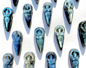 Könnte beinhalten: Eine Sammlung von irisierenden blau-grünen Labradorit-Göttinnen-Anhängern. Jeder Anhänger zeigt eine stilisierte weibliche Form mit einem Spiralmuster auf dem Torso. Die Anhänger sind auf weißem Hintergrund angeordnet.
