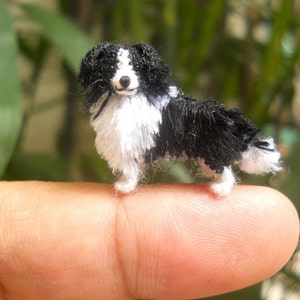 Puede incluir: Una pequeña figura de perro de crochet negro y blanco, de pie sobre un dedo.