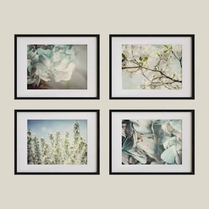 May include: Set of four framed floral art prints. Each print features a different close-up of flowers and foliage in soft, muted colors. The frames are black, and the prints have a white border.