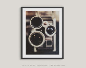 May include: Framed art print featuring a vintage camera with three lenses. The lenses are black with silver rims, and the image has a soft, blurred focus. The print is in a black frame and includes the text "LISA RUSSO FINE ART | SAMPLE DISPLAY | FRAME IS NOT INCLUDED."