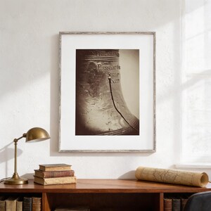 a framed photograph of a bell on a wall above a wooden desk with a lamp, books, and a map.