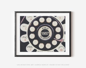May include: Close-up of a framed print featuring a vintage telephone dial. The dial is black with white numbers and letters, including "PUBLIC TELEPHONE 1957." The frame is black, and the image is displayed against a white background.