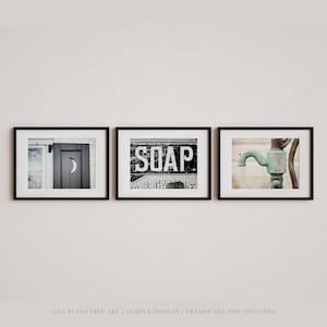May include: Set of three framed art prints. The first shows a black and white image of a door with a crescent moon cutout. The second print displays the word "SOAP" in bold letters. The third print features a close-up of a vintage water pump.