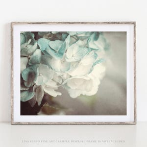 May include: A framed print featuring a close-up of hydrangea flowers in shades of blue and white. The flowers are in soft focus, with a vintage or antique aesthetic. The frame is a light wood color.