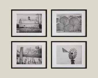 May include: Four framed black and white photographs. The images depict rural scenes: a barn, hay bales, a wooden fence, and a windmill. The photographs are mounted with white mounts.
