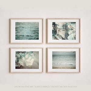 May include: Four framed art prints with a coastal theme. The prints feature images of water, ocean waves, and close-ups of blue and white hydrangea flowers. The frames are light-colored wood.
