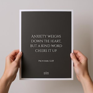 May include: A framed print with a dark gray background and white border. The text reads "ANXIETY WEIGHS DOWN THE HEART, BUT A KIND WORD CHEERS IT UP. PROVERBS 12:25." The words "ANCIENT ADVISOR" are at the bottom.