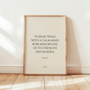 Może przedstawiać: Oprawiony wydruk z cytatem "TO BEAR TRIALS WITH A CALM MIND ROBS MISFORTUNE OF ITS STRENGTH AND BURDEN." autorstwa Seneki. Wydruk ma jasnobeżowe tło i drewnianą ramę. Tekst jest czarny.