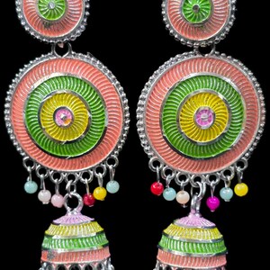 K&ouml;nnte beinhalten: Ein Paar farbenfrohe H&auml;ngeohrringe. Jeder Ohrring hat ein kreisf&ouml;rmiges Design mit konzentrischen Ringen in Rosa, Gr&uuml;n und Gelb. Kleine, bunte Perlen h&auml;ngen von unten, und die Ohrringe haben eine silberfarbene Metalloberfl&auml;che.