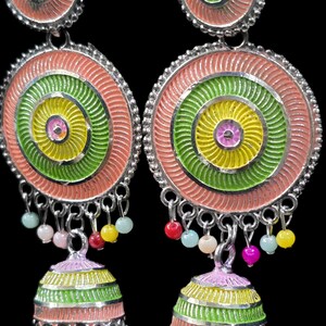 K&ouml;nnte beinhalten: Ein Paar bunte H&auml;ngeohrringe. Jeder Ohrring hat ein kreisf&ouml;rmiges Design mit konzentrischen Ringen in Rosa, Gr&uuml;n und Gelb. Kleine, farbige Perlen h&auml;ngen von unten, und die Ohrringe haben eine silberfarbene Metalloberfl&auml;che.