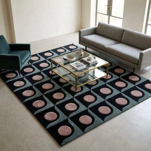 May include: A large area rug with a geometric pattern in black, teal, and dusty rose. The rug features a repeating design of circles within a square and curved shapes. The rug is placed in a living room setting with furniture.