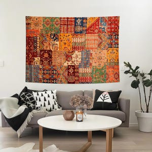 Op de afbeelding: Een grote, kleurrijke wandtapijt met een patchwork-ontwerp hangt aan een witte muur. Het wandtapijt heeft een verscheidenheid aan geometrische en bloemmotieven in tinten rood, oranje, blauw en groen. Een grijze bank met sierkussens en een witte salontafel staan ervoor.