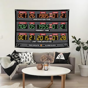 Puede incluir: Un gran tapiz de pared gris con una pantalla de tiempo digital con el texto "Destination Time", "Present Time" y "Last Time Departed". La pantalla muestra fechas y horas en naranja, verde y amarillo. El tapiz está colgado sobre un sofá gris.