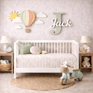 May include: A nursery scene featuring a white crib, a decorative hot air balloon, and the name "Jack" on the wall. A toy scooter, lamps, and a round rug complete the room's decor. The hot air balloon is in pastel colors.