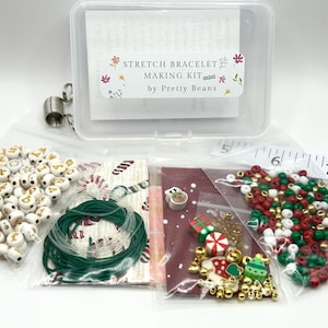 May include: A stretch bracelet making kit in a clear plastic container with a label reading STRETCH BRACELET MAKING KIT mini by Pretty Beans. Includes white letter beads, green elastic cord, red, green, and gold beads, and holiday charms.