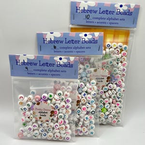 Op de afbeelding: Drie doorzichtige plastic zakken gevuld met witte Hebreeuwse letterkralen. Elke zak heeft een kop met de tekst "Hebrew Letter Beads" en het aantal complete alfabetsets. De kralen zijn in verschillende kleuren. De tekst "Pretty Beans alphabet beads" staat op een sticker.