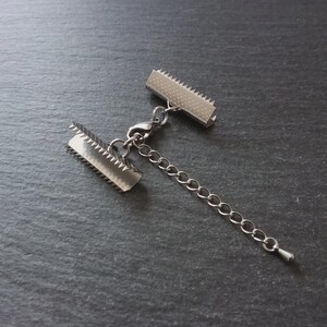 May include: A silver necklace clasp with two rectangular ends with serrated edges, linked by a chain. The clasp is for jewellery making and has a small lobster claw clasp.