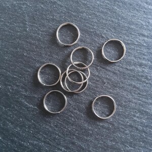 Pode incluir: Uma coleção de pequenos anéis de metal prateado espalhados sobre uma superfície cinza escuro. Os anéis são circulares e parecem ser feitos de um material metálico brilhante. Eles são provavelmente usados para chaveiros ou para fazer joias.