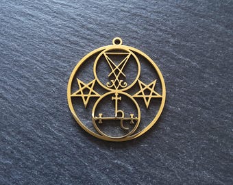 Könnte beinhalten: Ein goldfarbener Anhänger mit einem kreisförmigen Design und verschiedenen Symbolen. Der Anhänger enthält ein zentrales Symbol, zwei Sterne und andere geometrische Formen. Er hat eine kleine Schlaufe zum Aufhängen.