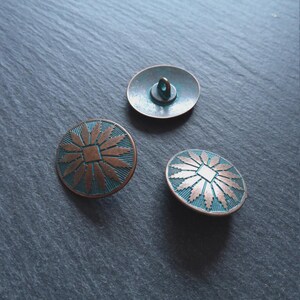 May include: Three antique copper buttons with a turquoise patina. Two have a circular sunburst design, and one is an oval with a loop. These buttons are likely for sewing or craft projects. The buttons are made of metal.