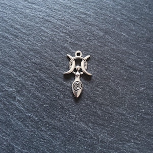 May include: A silver pendant depicting a female form with a spiral design, beneath a crescent moon and star symbol. The pendant has a small loop for hanging. The background is a dark, textured surface. The pendant is suitable for a necklace or charm bracelet.