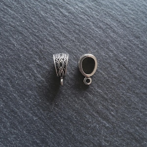 May include: Two silver pendant bails. One has an intricate woven pattern, the other is a simple oval with a small loop. These are designed for jewellery making and crafting projects.