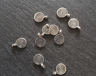 Puede incluir: Abalorios plateados en espiral con un lazo para sujetar a joyas u otras manualidades. Los abalorios están dispuestos sobre una superficie gris oscuro, con el diseño en espiral claramente visible. Ideales para crear collares, pulseras o pendientes únicos.