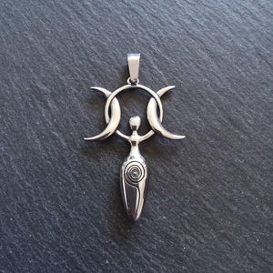 May include: A silver pendant with a woman design, a spiral on the torso, encircled by a ring and three crescent moons. The pendant is suspended from a small loop. The pendant is made of silver.