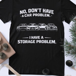 Puede incluir: Camiseta negra con el texto "NO, DON'T HAVE - A CAR PROBLEM. - I HAVE A - STORAGE PROBLEM." Cuatro ilustraciones de coches están encima del texto. La camiseta es una prenda informal.